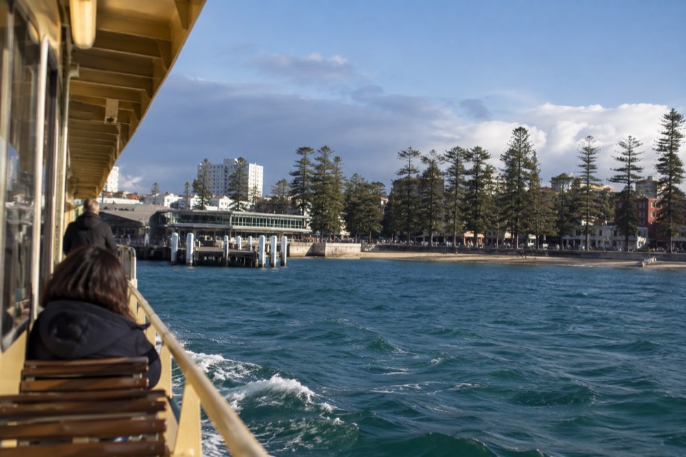 Manly ferry approaching the wharf with beachfront promenade beyond