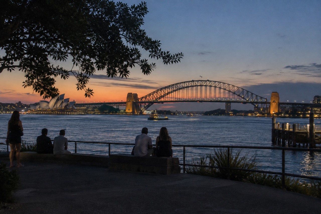 Sydney Harbour at dusk with the Opera House and Harbour Bridge lit against a summer sky
