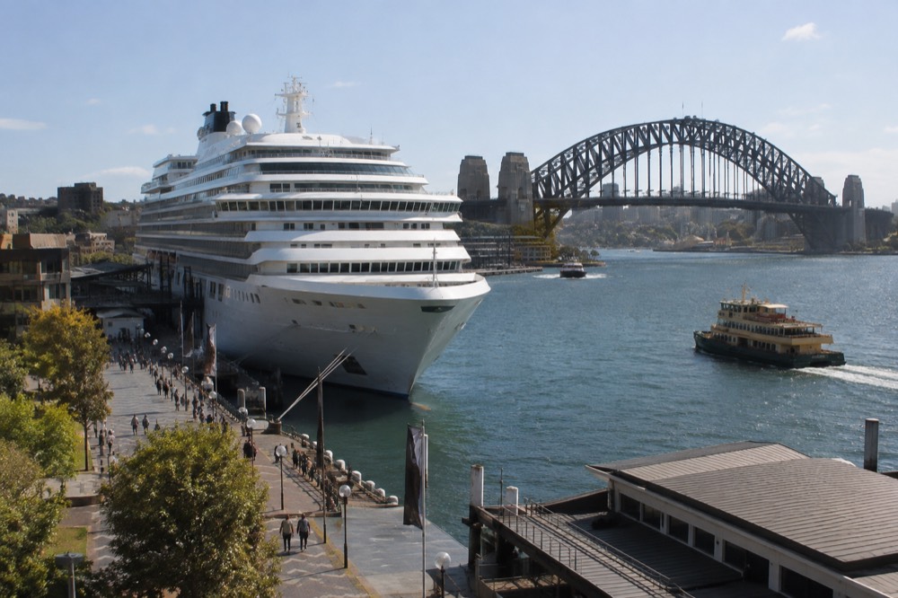 A cruise ship moored at a stone quay with a steel arch bridge rising behind it