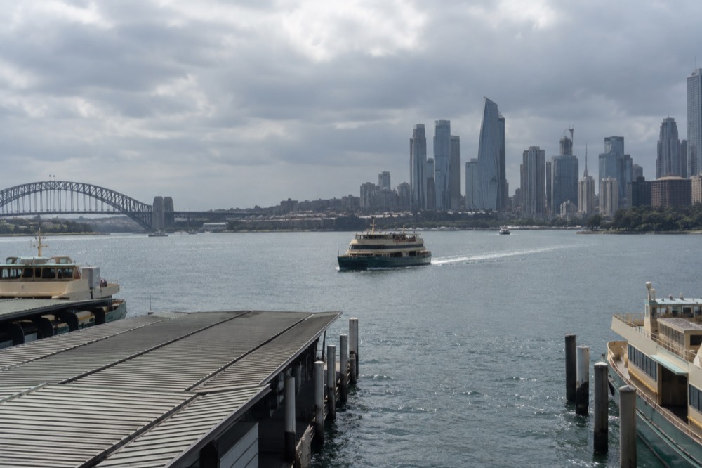A ferry crossing a sunlit harbour toward a city skyline of towers