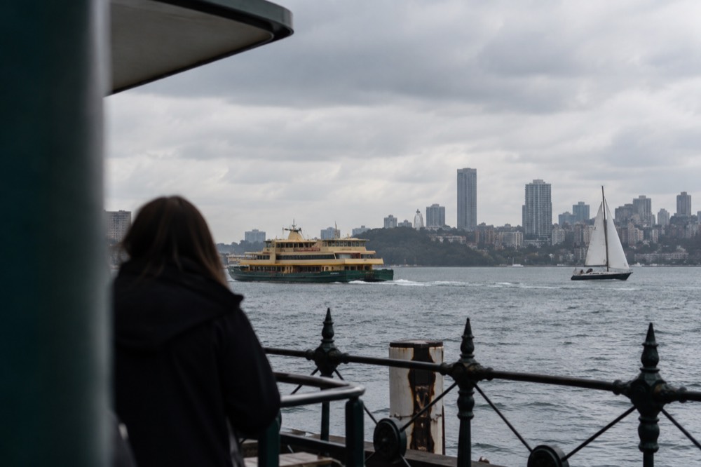 A sailing boat and ferry on open harbour water with the city skyline behind