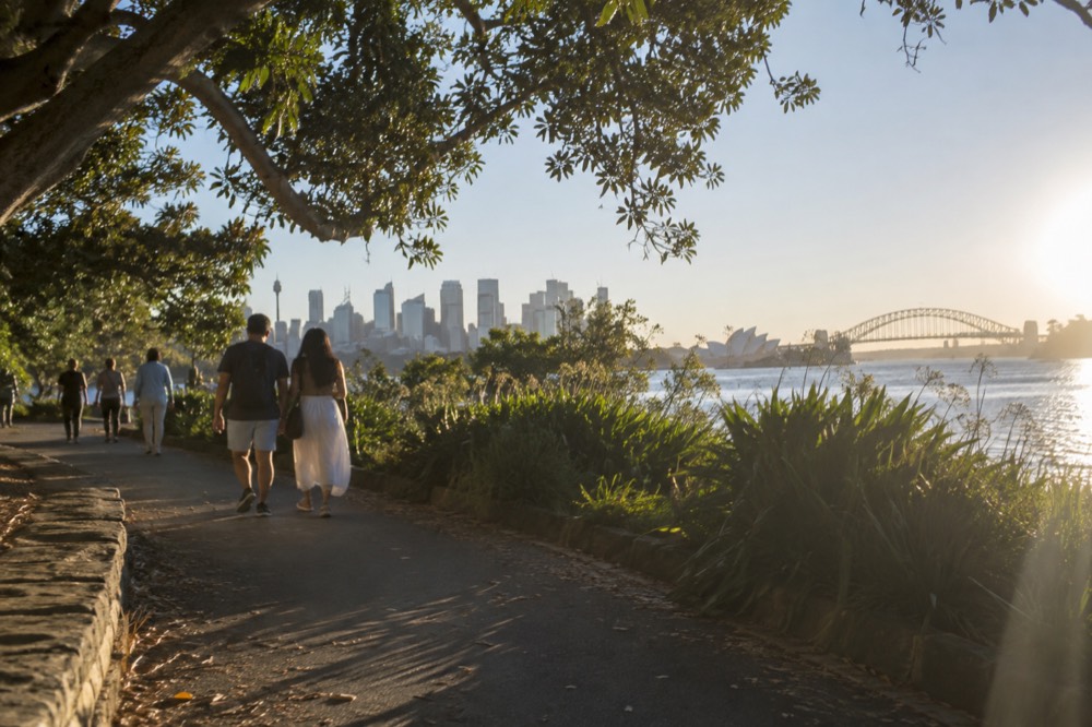 Visitors walking through the Royal Botanic Garden toward the city skyline